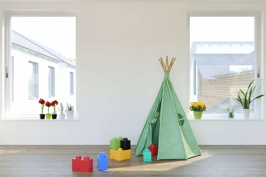 jasny pokój dziecięcy z dwoma dużymi białymi oknami, zielonym namiotem tipi i klockami na podłodze
