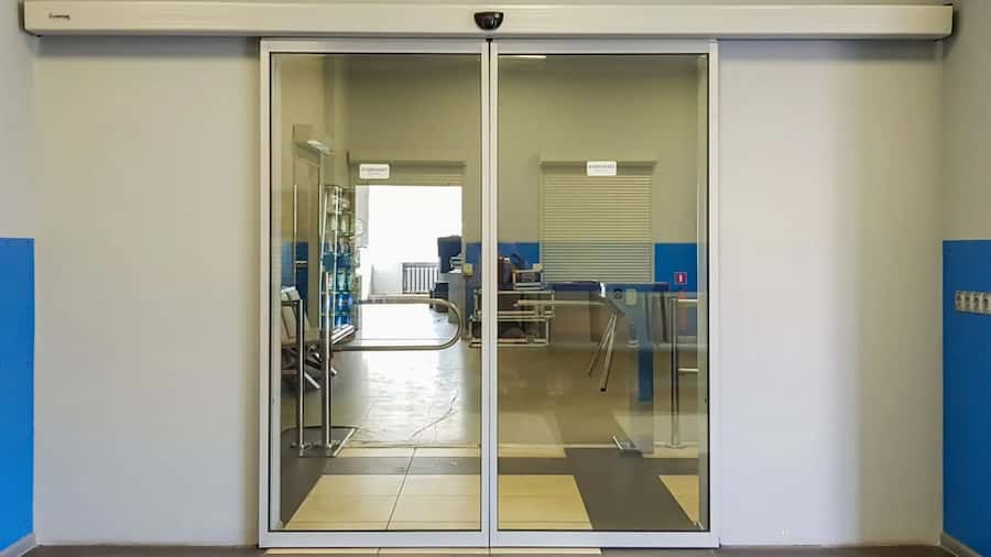 automatyczne drzwi przesuwne z białym profilem i widocznym napędem z czujnikiem wewnątrz pomieszczenia