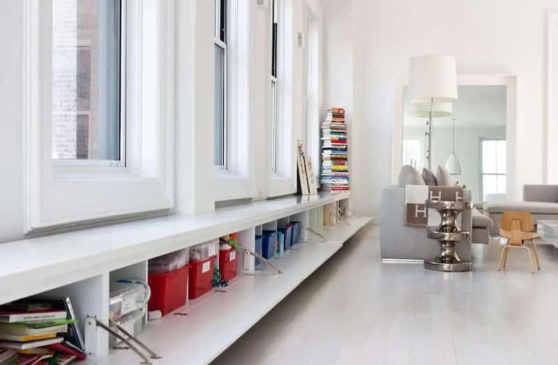wykorzystanie szerokiego białego parapetu jako funkcjonalnej półki na książki i strefy wypoczynku w jasnym, nowoczesnym wnętrzu