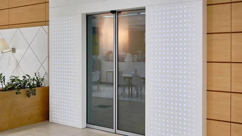 wbudowane automatyczne drzwi przesuwne z czujnikiem ruchu w minimalistycznym wnętrzu z panelami drewnianymi