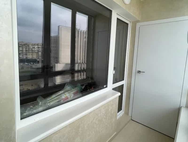 zabudowany balkon z wykorzystaniem ciemnego profilu okiennego i białych drzwi wewnętrznych w jasnym wnętrzu