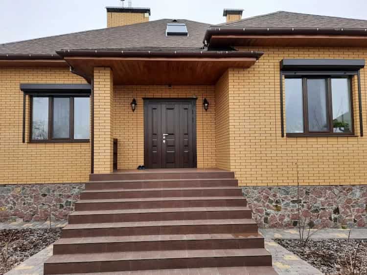 okna PCV w ciemnobrązowej okleinie ze zintegrowanymi roletami zewnętrznymi na elewacji z cegły