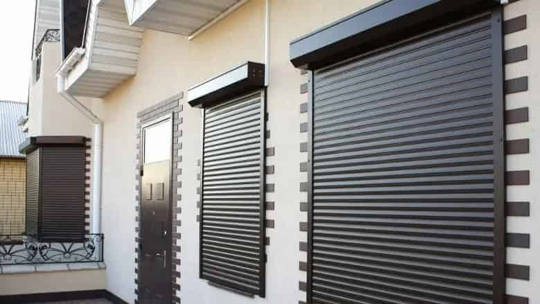 zewnętrzne rolety zabezpieczające w kolorze brązowym, zamontowane na oknach i drzwiach wejściowych domu prywatnego